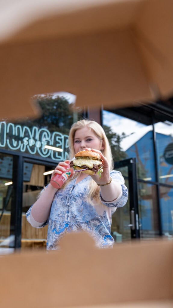 Kvinne med burger utenfor en kafé i Oslo, fokus på mat og byliv.